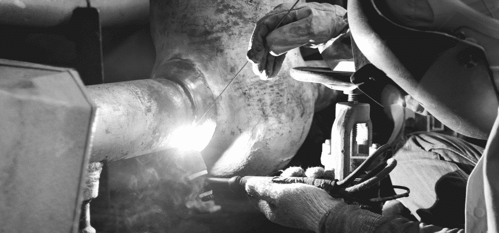 Welder wearing full protective equipment including helmet, jacket and insulated gloves while welding a pipe